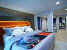 Modern bedroom with decorative pillows and bedspread, featuring a view into another bedroom through a glass partition.