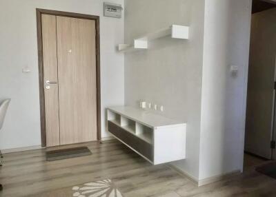 Entryway with a wooden door, white walls, and a floating shelf