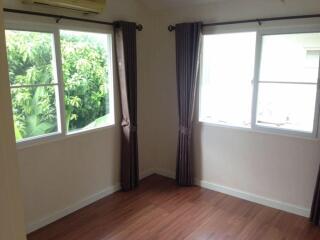 A well-lit bedroom with hardwood floors, large windows, and brown curtains.