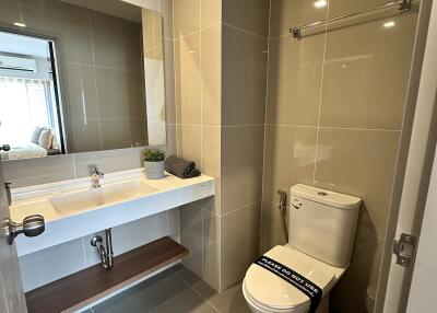 Modern bathroom with toilet, sink, mirror, and light brown tiled walls.