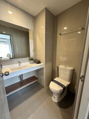 Modern bathroom with toilet, sink, mirror, and light brown tiled walls.