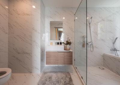 Modern bathroom with glass shower, bathtub, sink, and toilet