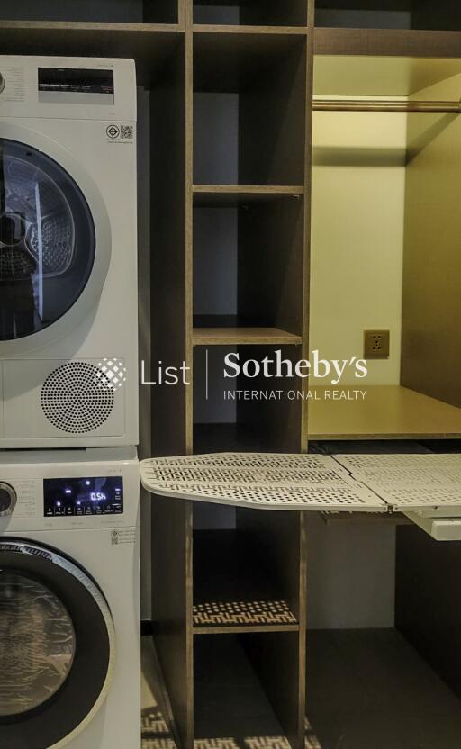 Laundry room with stacked washer and dryer, ironing board, and storage shelves