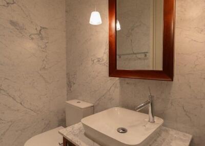 Modern bathroom with marble walls and countertop, mirror, and suspended lights