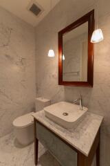 Modern bathroom with marble walls and countertop, mirror, and suspended lights