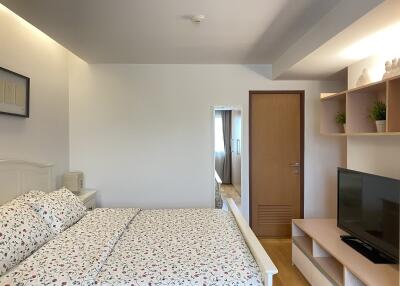 Modern bedroom with bed, closed door, shelves, and television