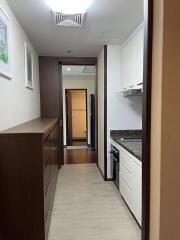 A narrow kitchen with cabinets, granite countertops, and a view into the hallway and bathroom.