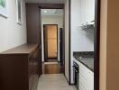 A narrow kitchen with cabinets, granite countertops, and a view into the hallway and bathroom.