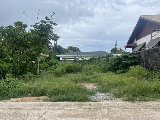 Vacant lot with greenery and houses in the background