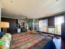 Spacious bedroom with colorful bedspread, large windows, and balcony access.