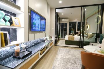 Modern living room with TV, open shelving, and view into a bedroom with glass partitions