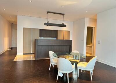 Modern dining area with a glass table and upholstered chairs, open to a kitchen with a breakfast bar.