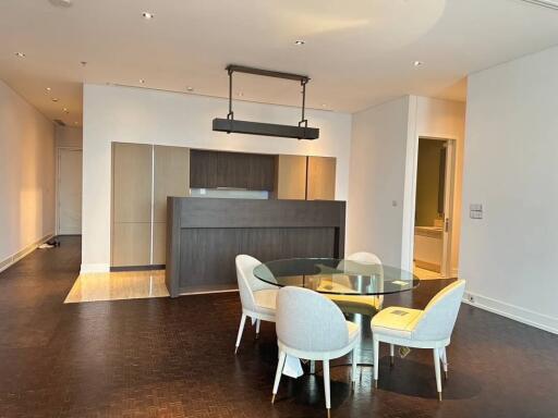 Modern dining area with a glass table and upholstered chairs, open to a kitchen with a breakfast bar.