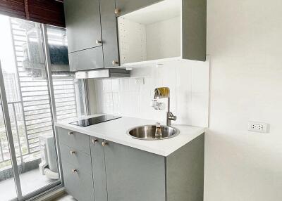 Compact modern kitchen with grey cabinets, sink, stovetop, and balcony access