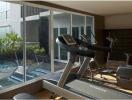 Modern gym with exercise equipment next to large windows overlooking an outdoor pool area