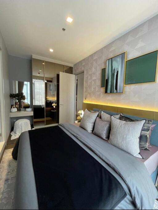 Modern bedroom with a cozy bed, decorative pillows, artwork, and a mirrored wardrobe