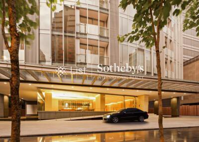 Modern high-rise building with illuminated entrance and parked car at dusk