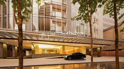 Modern high-rise building with illuminated entrance and parked car at dusk