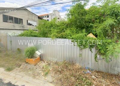 Vacant lot with overgrown vegetation and a metal fence