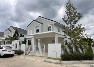 Front view of a modern white house with a car parked in front and greenery