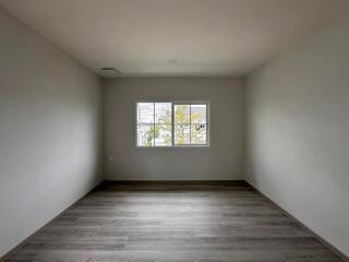 Spacious empty bedroom with wooden flooring and a large window