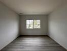 Spacious empty bedroom with wooden flooring and a large window