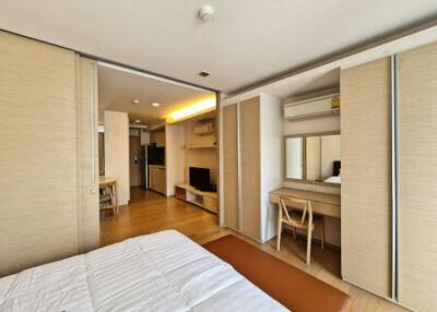 Modern bedroom with a view of living and kitchen areas, featuring wooden furniture and ample storage