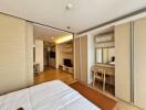 Modern bedroom with a view of living and kitchen areas, featuring wooden furniture and ample storage