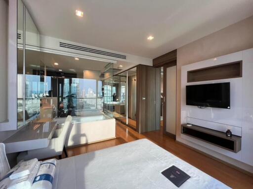 Modern bedroom with city view, glass walls, and TV