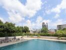 Outdoor swimming pool area with lounge chairs and greenery, under a blue sky with clouds