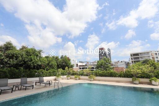 Outdoor swimming pool area with lounge chairs and greenery, under a blue sky with clouds