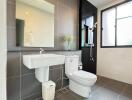 Modern bathroom with grey tiles, sink, toilet, and shower