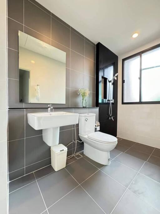 Modern bathroom with grey tiles, sink, toilet, and shower