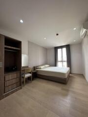 A minimalist bedroom with wooden flooring, a bed, a wardrobe, and a window with curtains.