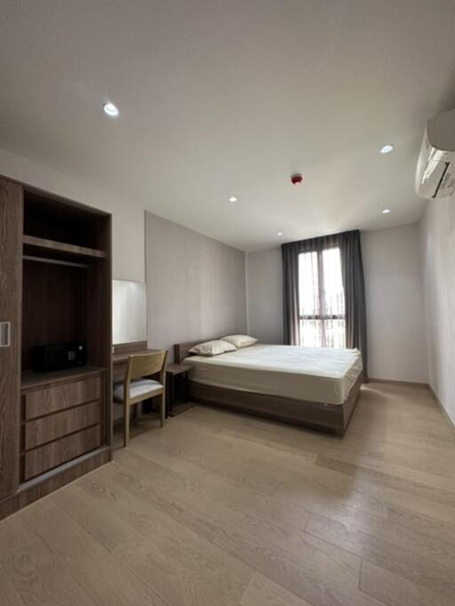 A minimalist bedroom with wooden flooring, a bed, a wardrobe, and a window with curtains.