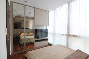 Modern bedroom with large windows, mirrored wardrobe, and a mounted TV