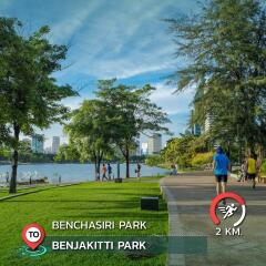 People jogging and walking in an urban park with trees, a lake, and distant city buildings