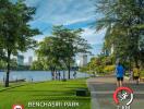 People jogging and walking in an urban park with trees, a lake, and distant city buildings