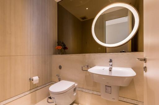 Modern bathroom with a round-lit mirror, sink, and toilet