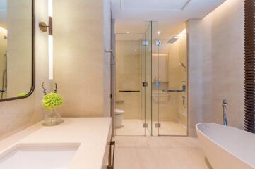 Modern bathroom with glass shower, bathtub, and lighted mirror