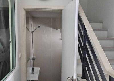 Small bathroom under stairs with sink, shower, and wall-mounted clock