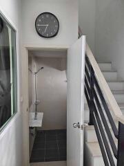 Small bathroom under stairs with sink, shower, and wall-mounted clock