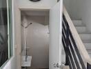 Small bathroom under stairs with sink, shower, and wall-mounted clock