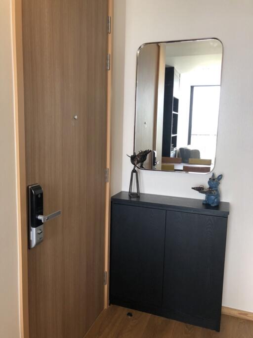 Apartment entrance with modern wooden door, black cabinet, decorative items, and mirror