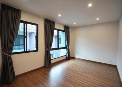 Empty bedroom with wooden flooring, curtains, and windows