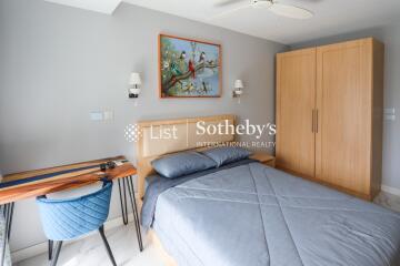 Bedroom with modern wooden wardrobe and bed, desk, blue chair, painting on the wall, and overhead lighting