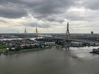 View of a river with a bridge and buildings in the background under a cloudy sky