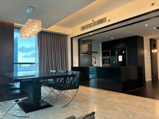 Modern dining area with chandelier, adjacent to an open kitchen.