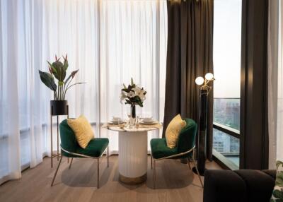 A cozy dining area with a round table set for two, green velvet chairs, and large windows