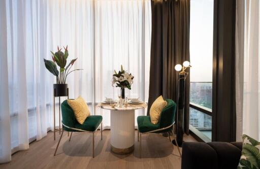 A cozy dining area with a round table set for two, green velvet chairs, and large windows